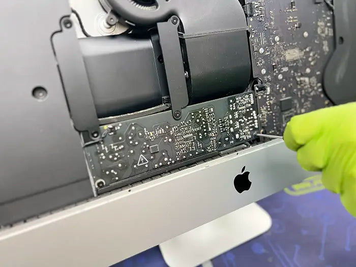 A Prime Tech Support technician delicately uses a screwdriver to take apart the iMac computer and examine the power supply for any possible problems. Once identified, they will proceed with the required repairs.