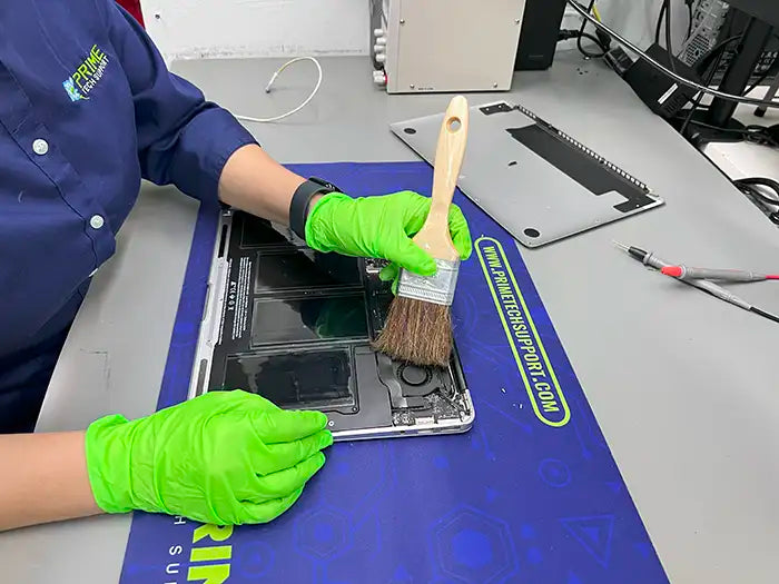 The technician in Miami employs a brush to clean the fans and internal components of the MacBook Air, ensuring optimal performance for the client.