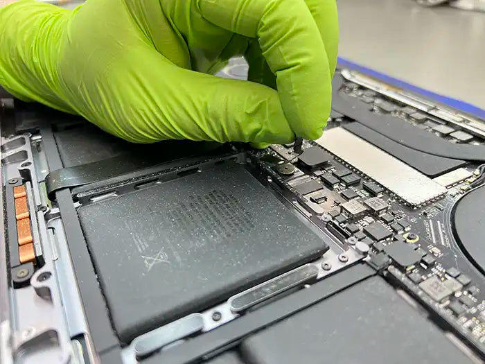 Prime Tech Support Technician wearing gloves and carefully detaching the flex of a MacBook Pro Battery to replace it our lab in Miami