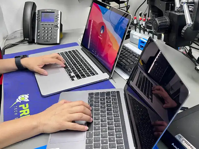 Prime Tech Support technician using two laptops in order to perform a data transfer service for a MacBook Pro client in our specialized lab in Miami