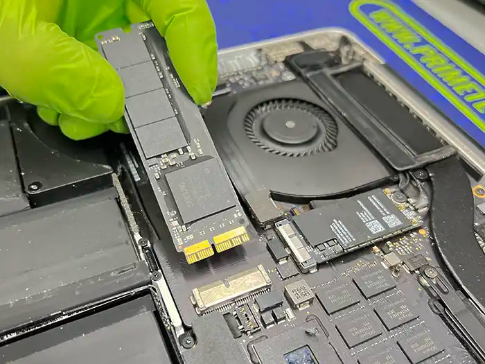 At Prime Tech Support's specialized lab in Miami, a technician wearing green gloves expertly carries out a hard drive replacement for a MacBook Pro.