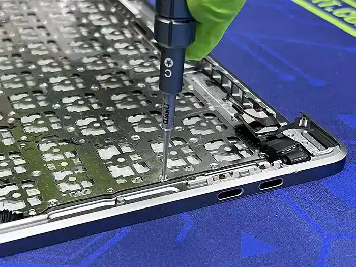 In Prime Tech Support's specialized lab in Miami, a technician is carrying out a MacBook keyboard replacement service. They carefully inspect the keyboard and use a screwdriver to disassemble it.