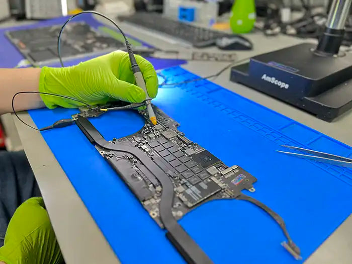 In Prime Tech Support's specialized lab located in Miami, a technician carefully inspects and repairs a logic board. The technician is testing and examining the logic board to identify any issues and perform the necessary repairs.