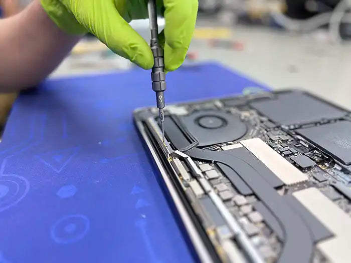 Prime Tech Support technician wearing green gloves and using a screwdriver to dissemble the rear part of the MacBook Pro to examine the possible screen damage