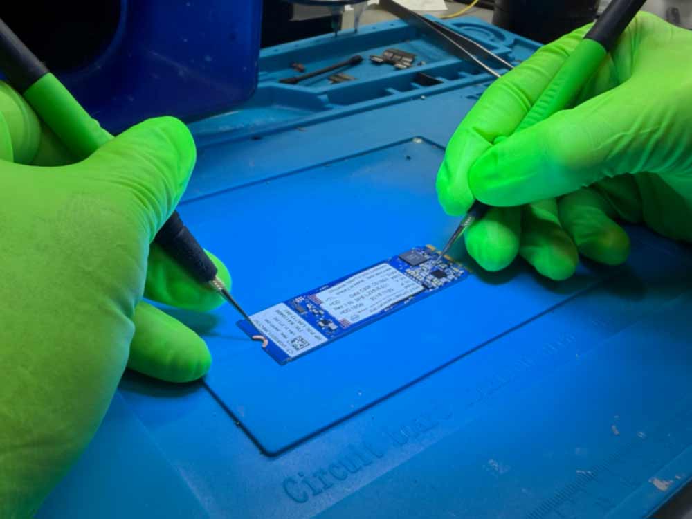 NVMe data recovery work showing a technician handling an NVMe SSD circuit board using precision tools in a lab environment.