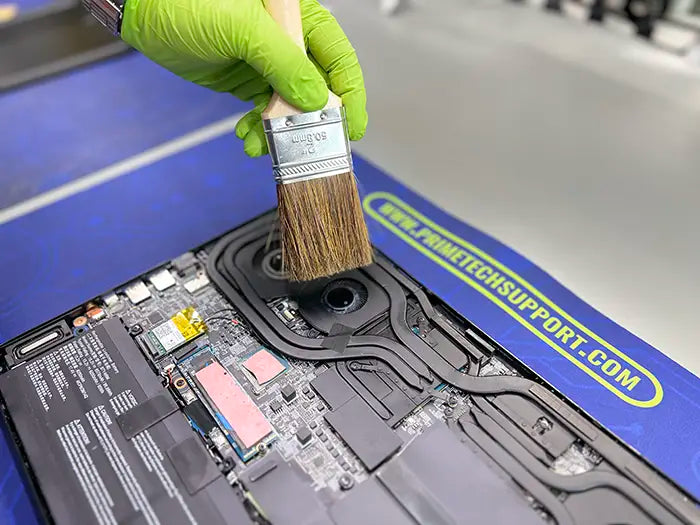 The technician carefully uses a brush to deeply clean the fans and internal components of the gaming laptop, ensuring it performs at its best.