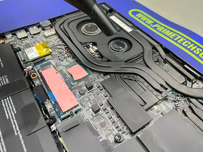 The technician employs an air cleaning tool to thoroughly cleanse the fans and internal components of the gaming laptop, ensuring optimal performance.