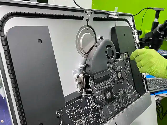 In the specialized lab of Prime Tech Support located in Miami, a technician is repairing the logic board of an iMac using a screwdriver for a client.