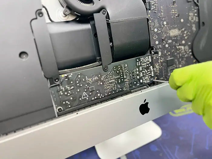  A Prime Tech Support technician delicately uses a screwdriver to take apart the iMac computer and examine the power supply for any possible problems. Once identified, they will proceed with the required repairs.
