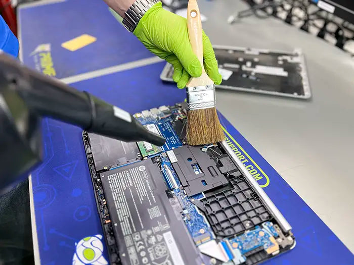 Technician using a brush and air cleaning tool to deeply clean and dust a laptop in the lab in Miami