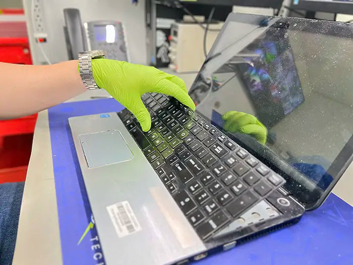In the Prime Tech Support lab located in Miami-Dade County, a technician removes a laptop keyboard to replace it for a client's device.