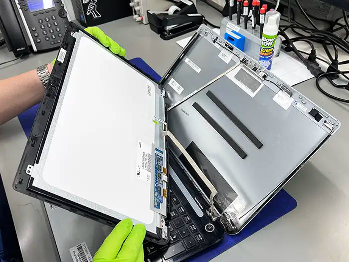 In Miami, a Prime Tech Support technician, wearing green gloves, carefully removes the damaged screen of a laptop to inspect and repair it for a customer.