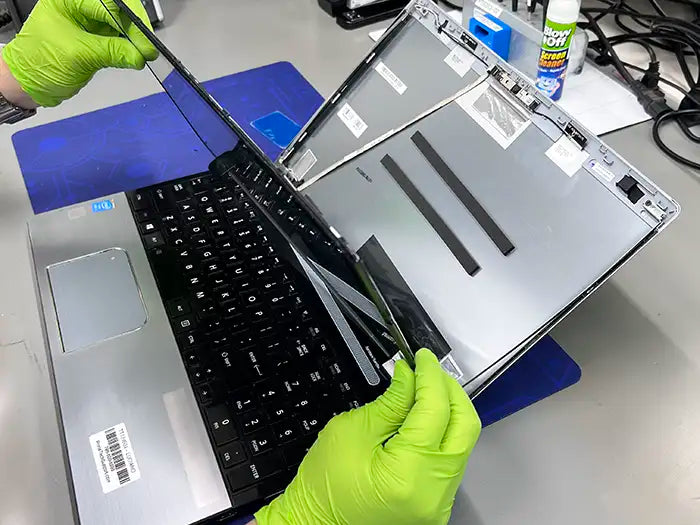 Prime Tech Support technician wearing green gloves and detaching the damaged screen of a laptop to inspect it and repair it for a customer located in Maimi