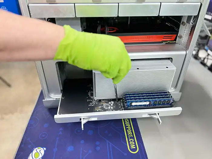 Prime Tech Support technician wearing green gloves and using a screwdriver to dissemble a Mac Pro computer to examine it and find the cause of the problems in Miami Lab