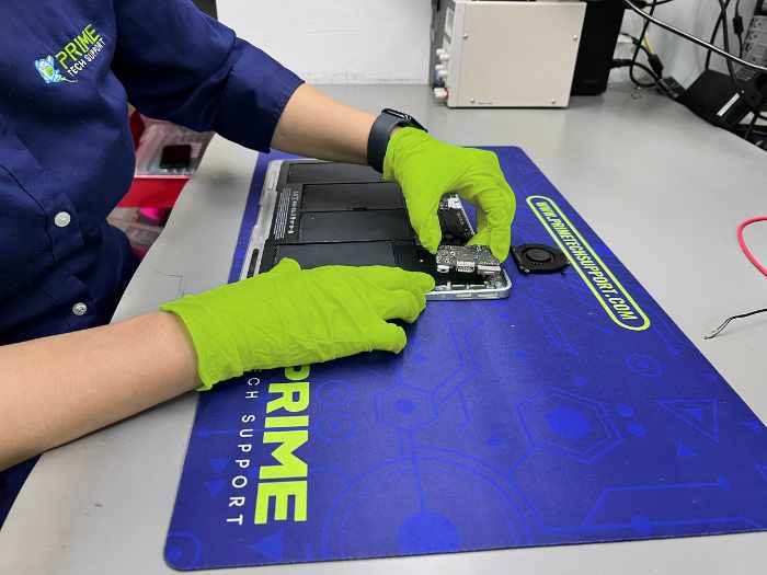 Prime Tech Support technician wearing green gloves and using some tweezers to examine a remove the DC Jack component of a MacBook Air in our specialized lab in Miami