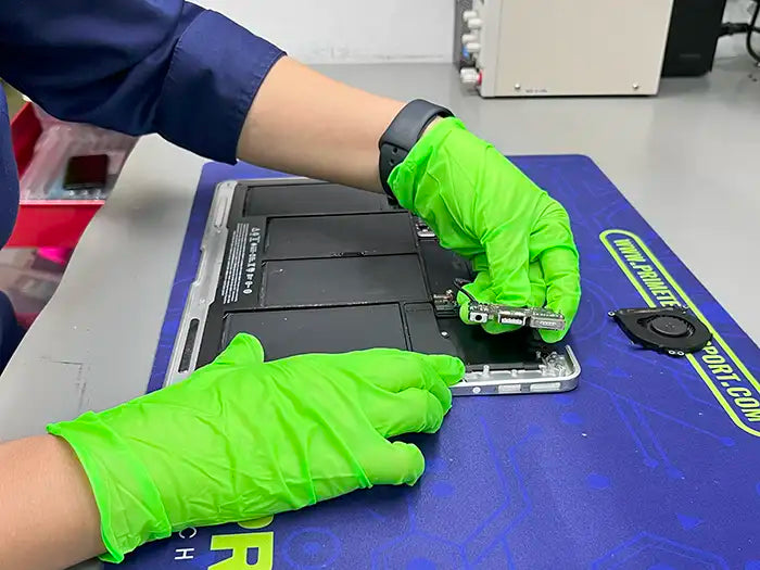 Prime Tech Support technician wearing green gloves and using some tweezers to examine a remove the DC Jack component of a MacBook Air in our specialized lab in Miami