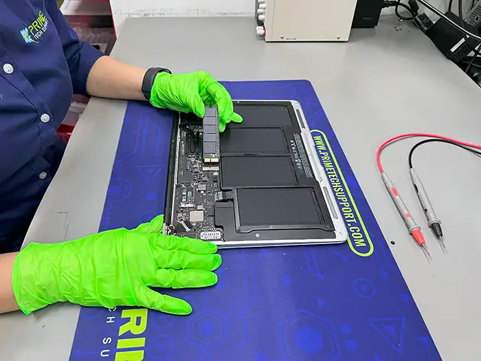  At Prime Tech Support's specialized lab in Miami, a technician wearing green gloves expertly carries out a hard drive replacement for a MacBook Air.