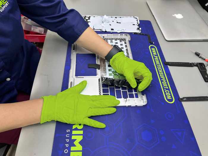 Prime Tech Support technician wearing green gloves and detaching the keyboard of a MacBook Air for a customer located in Miami