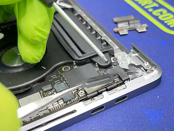 Inside Prime Tech Support's specialized lab in Miami, a technician, wearing green gloves and employing a screwdriver, meticulously removes the DC Jack component from a MacBook Pro.
