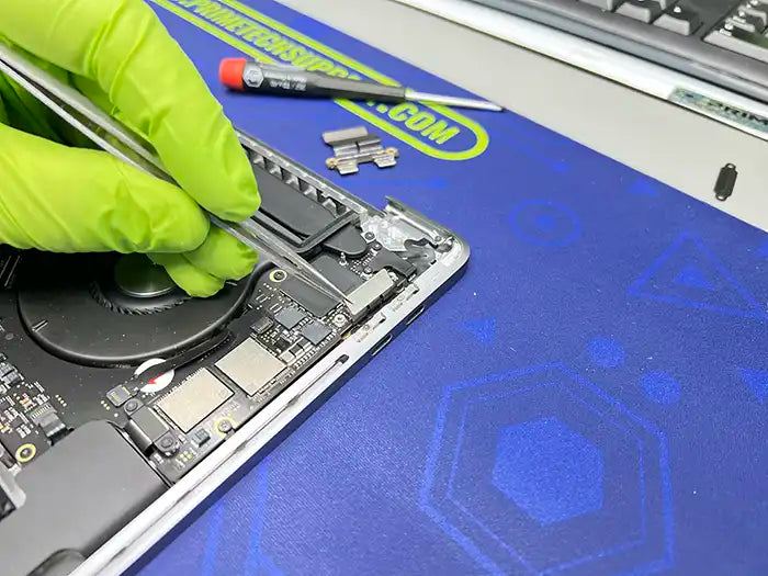 Prime Tech Support technician wearing green gloves and using some tweezers to examine a remove the DC Jack component of a MacBook Pro in our specialized lab in Miami