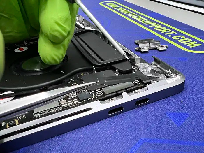 In Prime Tech Support's specialized lab in Miami, a technician wearing green gloves and using a screwdriver diligently removes the DC Jack component of a MacBook Pro.