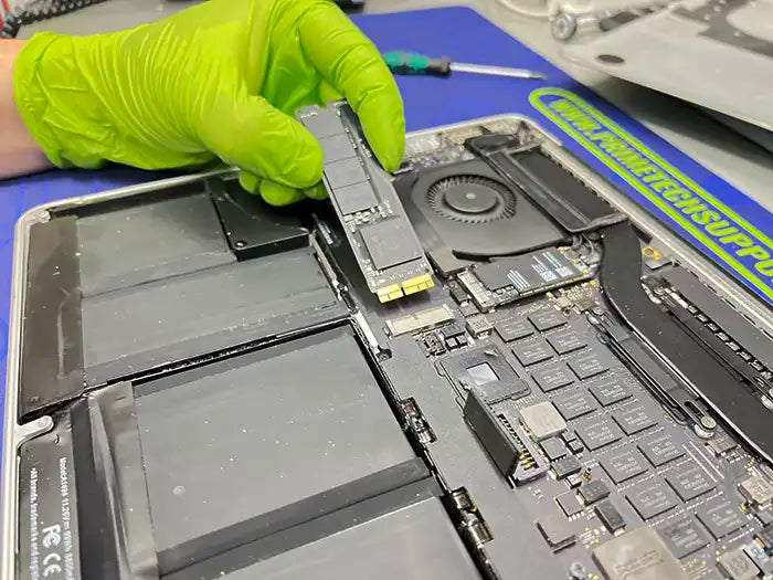 Prime Tech Support Technician wearing green gloves and performing a hard drive replacement in Miami specialized lab for a MacBook Pro