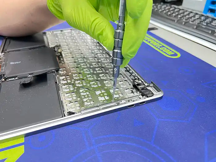 MacBook keyboard replacement service is being performed in Prime Tech Support specialized lab located in Miami. The technician is examining the keyboard and using a screwdriver to disassemble it 