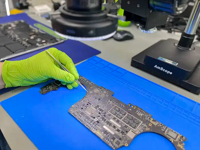 MacBook Pro liquid damage service performed by computer technician in specialized lab located in Miami. He is using professional tools like a microscope to closely examine the damage caused by the liquid to the MacBook Pro