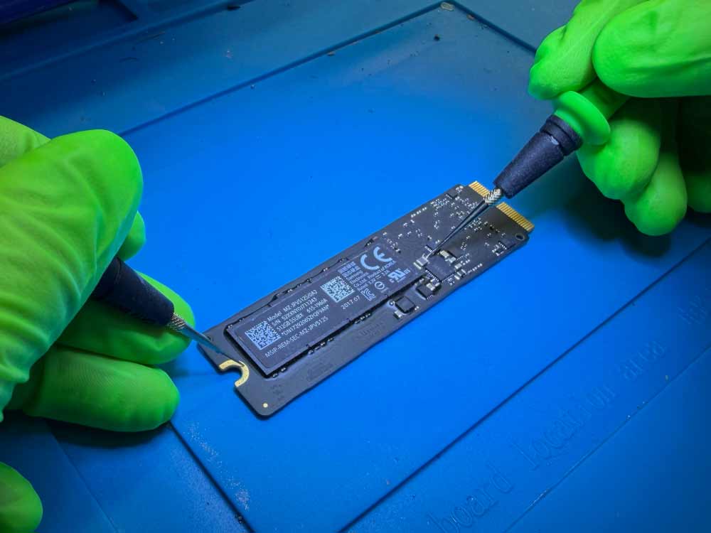 MacBook Pro SSD data recovery work showing a technician handling an Apple SSD using precision tools on a lab workbench.