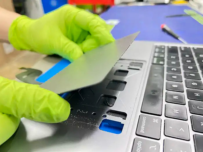 Prime Tech Support technician wearing green gloves dissembling a Miami customer's MacBook Pro trackpad to replace it.