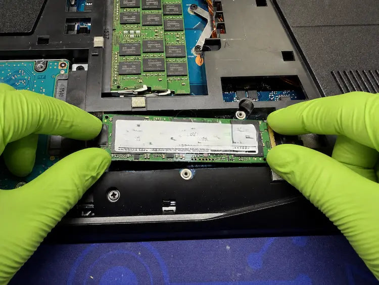 Técnico con guantes verdes diagnosticando un SSD NVMe dentro de un portátil para solucionar el rendimiento lento del sistema