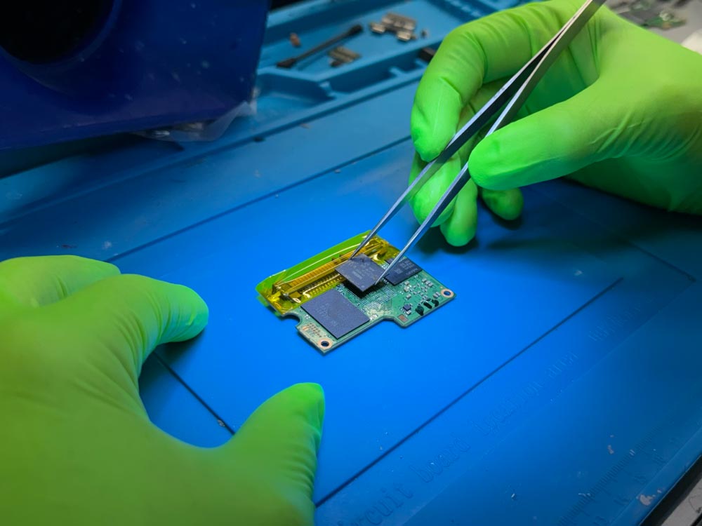 SSD data recovery work showing a technician handling flash memory components on an SSD board under magnification.