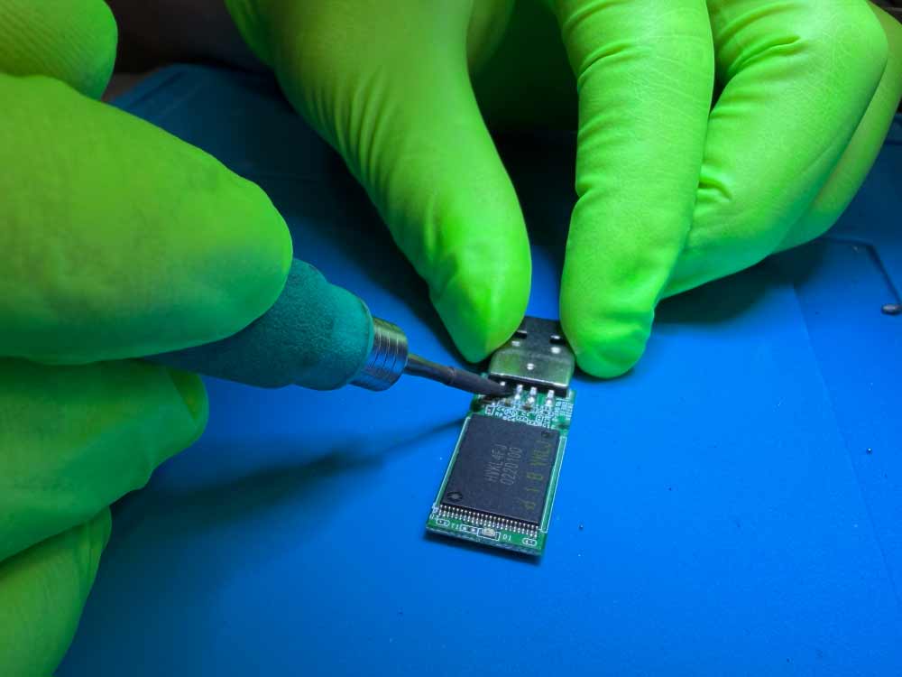 USB flash drive data recovery showing a technician microsoldering components on a USB circuit board in a lab environment.